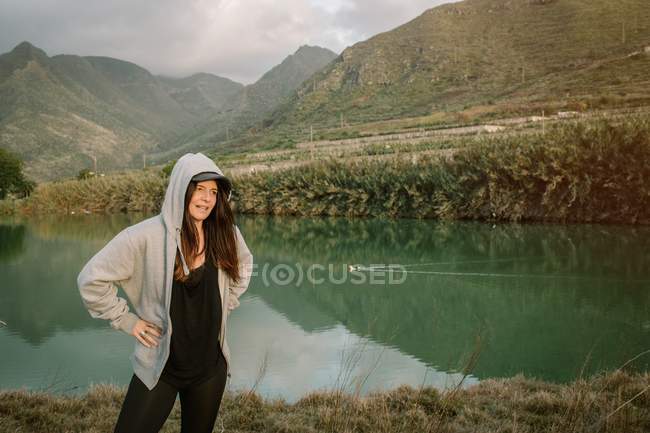 Mulher positiva ter uma pausa depois de correr na natureza perto do lago e montanhas — Fotografia de Stock