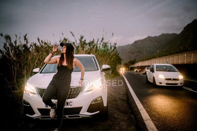 Woman drinking water from bottle near car on road at dusk — Stock Photo