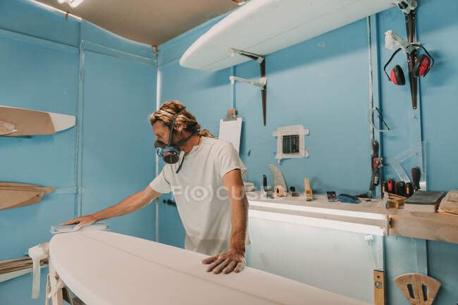 Uomo in respiratore lucidatura tavola da surf in officina — Foto stock