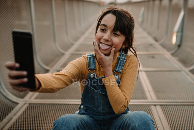 Menina alegre tomando selfie com smartphone em passarela de metal — Fotografia de Stock