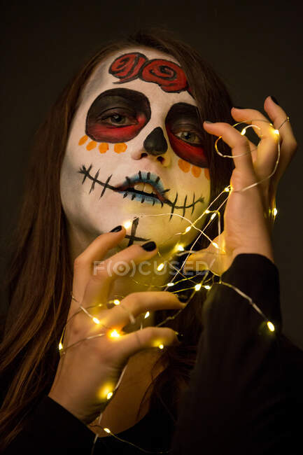 Jeune femme avec une peinture effrayante sur le visage tenant des lumières de fées — Photo de stock