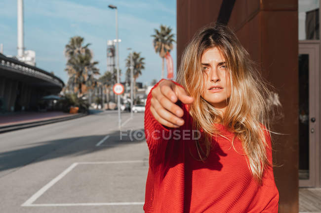 Sinnliche geheimnisvolle junge Dame im roten Pullover mit ausgestreckter Hand, die auf der Straße vor verschwommenem Hintergrund steht — Stockfoto