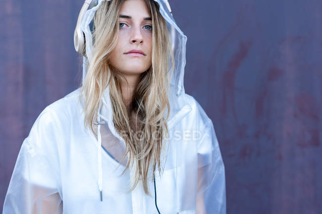 Portrait of cool stylish woman in raincoat sitting looking at camera in front of wall — Stock Photo