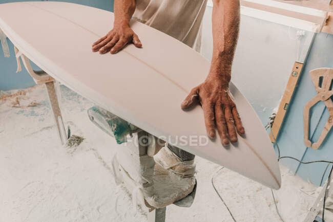 Crop male tenant une planche de surf en bois placée sur le stand sur le lieu de travail — Photo de stock