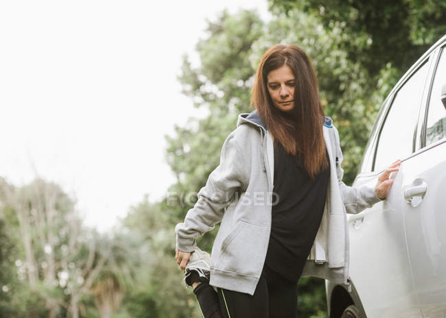 Femme en tenue de sport s'étirant près de la voiture dans le parc — Photo de stock
