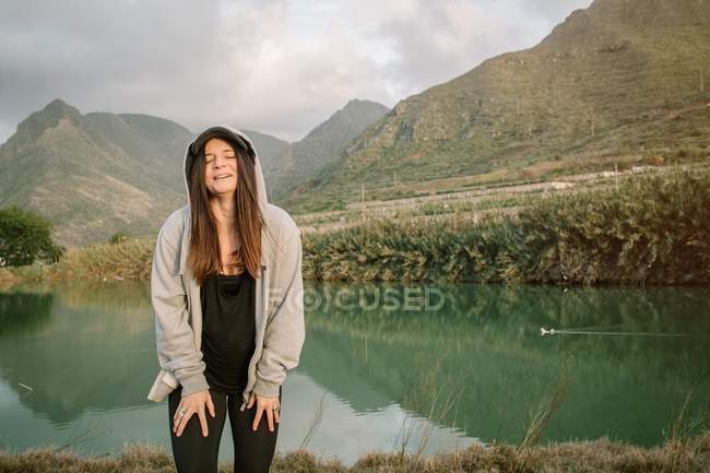 Positive Frau macht Pause nach dem Laufen in der Natur in der Nähe von See und Bergen — Stockfoto