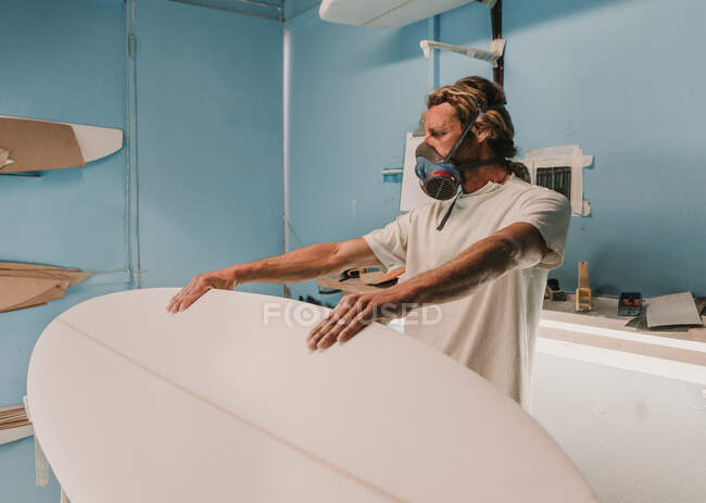 Человек держит доску для серфинга на стенде в мастерской — стоковое фото