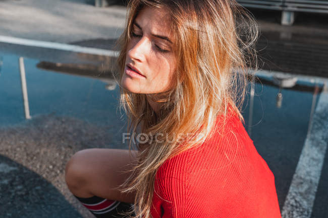 Sensual young lady in red sweater sitting on road between puddles — Stock Photo