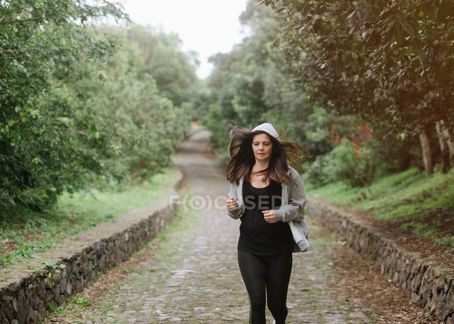 Positive woman in sportswear running on pathway in park — Stock Photo
