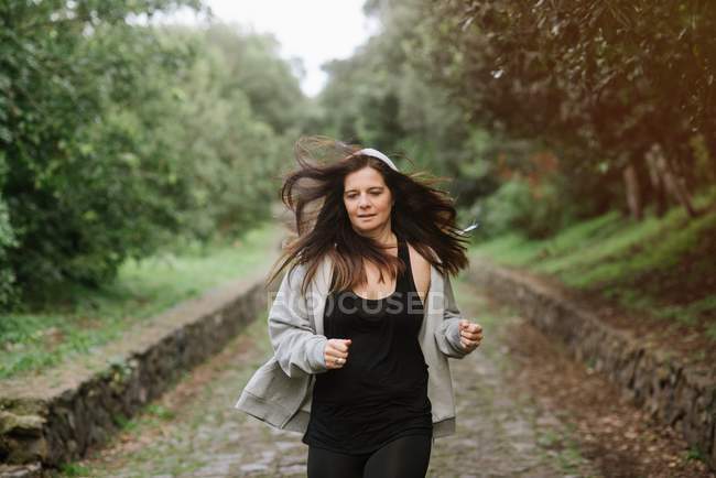 Mulher positiva em sportswear correndo no caminho no parque — Fotografia de Stock