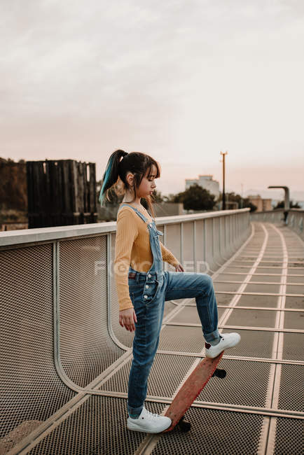 Дівчина стоїть зі скейтбордом на металевій прогулянці в місті — стокове фото
