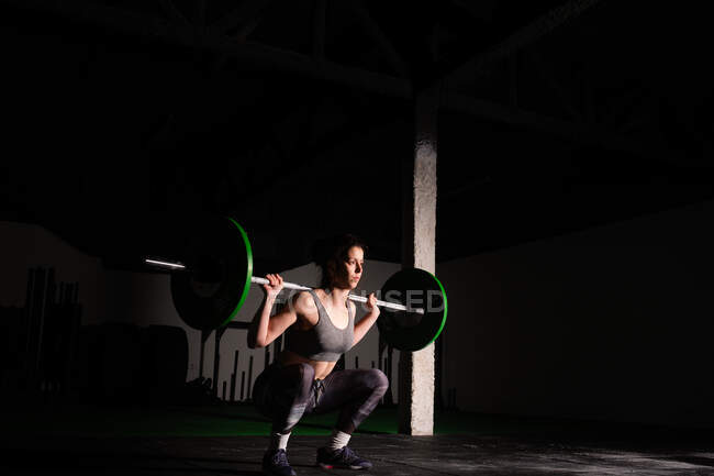 Athlétique jeune femme concentrée dans les vêtements de sport upping barbell au-dessus de la tête dans la salle de gym — Photo de stock