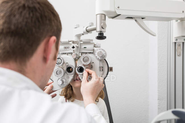 Opticida testando os olhos de uma menina com dispositivos de optometria — Fotografia de Stock