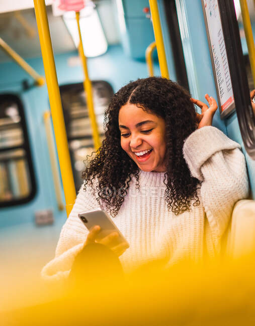 Felice attraente giovane signora afro-americana con capelli ricci navigazione sul telefono cellulare nel veicolo di servizio pubblico — Foto stock