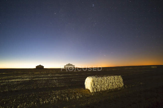 Paisagem de campos com feno de palha e edifícios no fundo sob céu estrelado à noite — Fotografia de Stock