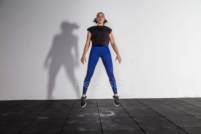 Atlética joven concentrada dama en ropa deportiva haciendo sentadillas y saltar en el gimnasio - foto de stock