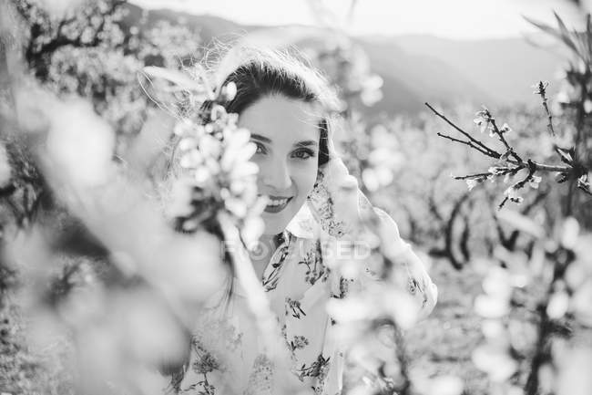 Zweige blühender Obstbäume fröhliche Dame blickt in Kamera im Garten — Stockfoto