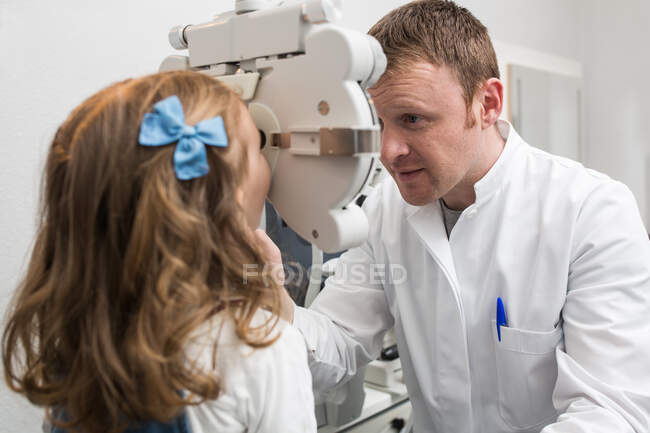 Opticida testando os olhos de uma menina com dispositivos de optometria — Fotografia de Stock