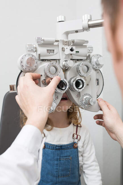 Óptico probando los ojos de una chica con dispositivos de optometría - foto de stock