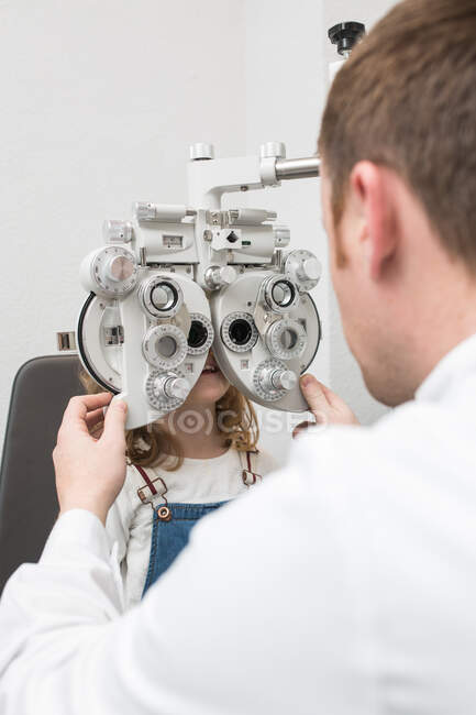 Opticien testant les yeux d'une fille avec des dispositifs d'optométrie — Photo de stock