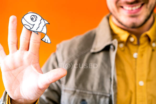 Happy guy showing paper silhouette for April fools day on orange blurred background — Stock Photo