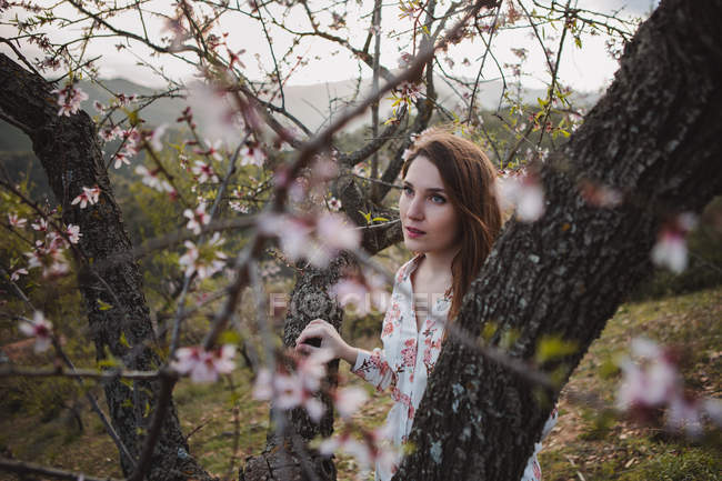 Ramoscelli di albero da frutto in fiore e giovane donna che guarda lontano nella natura — Foto stock
