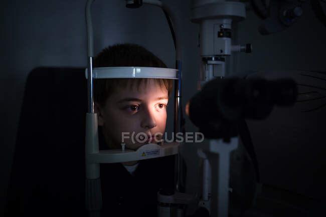 Оптик тестирует глаза мальчика с помощью оптических приборов — стоковое фото