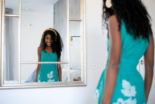 Black teenage girl with curly hair smiling looking at camera in front of a  mirror listening to music in headphones — leisure, african american - Stock  Photo | #251670272