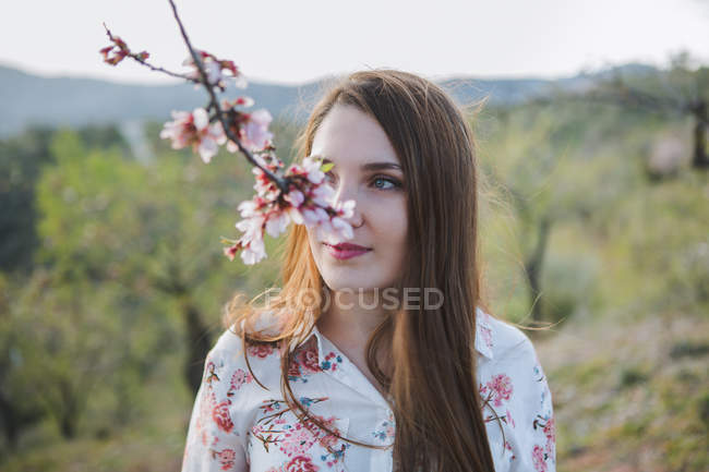 Веточка цветущего фруктового дерева и заботливая молодая женщина, смотрящая вдаль на природу — стоковое фото
