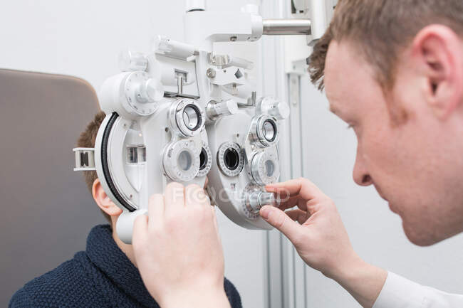 Opticida testando os olhos de um menino com dispositivos de optometria — Fotografia de Stock