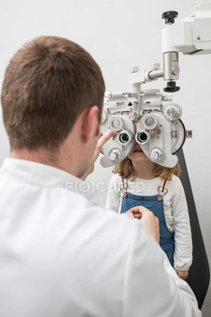 Óptico probando los ojos de una chica con dispositivos de optometría - foto de stock