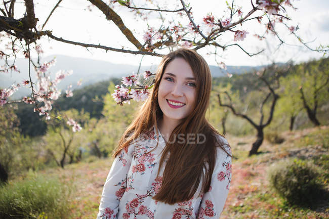 Портрет веселой юной леди, смотрящей на камеру в саду с цветущим фруктовым деревом — стоковое фото