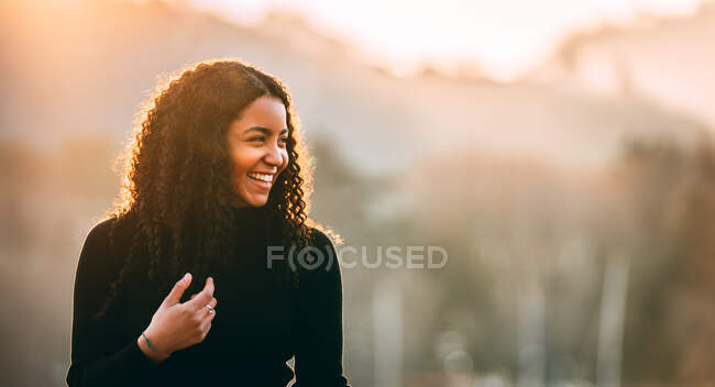 Feliz joven y atractiva dama afroamericana mirando hacia otro lado sobre un fondo borroso - foto de stock