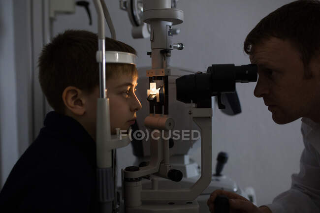 Оптик тестирует глаза мальчика с помощью оптических приборов — стоковое фото