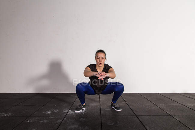 Athletic young concentrated lady in sportswear doing squats in gym — Stock Photo