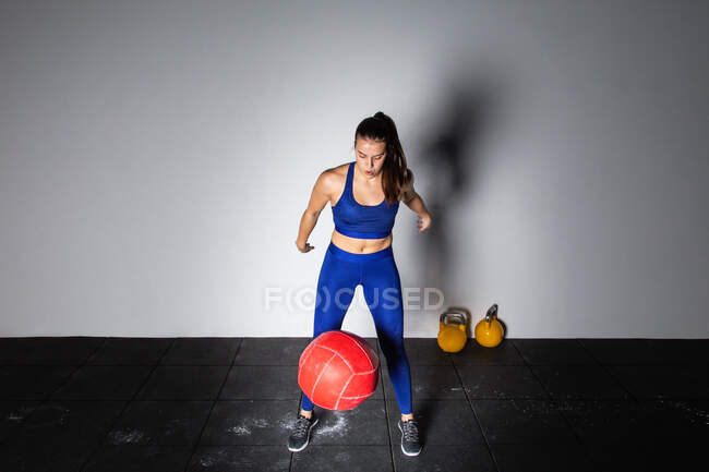 Athletic young concentrated lady in sportswear in chalk upping heavy medicine ball on shoulder in gym — Stock Photo