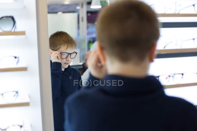 Lindo chico joven probándose gafas en una tienda de gafas - foto de stock