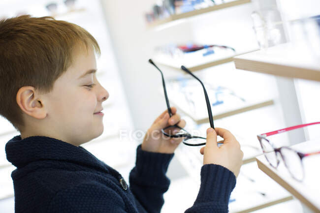 Милий молодий хлопчик приміряє окуляри в магазині одягу — стокове фото