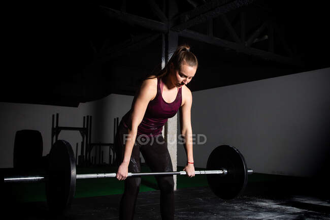 Спортсменка молода концентрована леді в спортивному одязі збільшується барбелл над головою в спортзалі — стокове фото