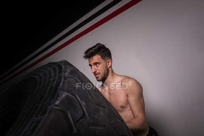Atletico giovane ragazzo senza maglietta avendo concorrenza di capovolgere grandi pneumatici in palestra — Foto stock