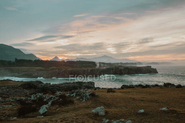 Vue pittoresque de la haute côte près de la mer orageuse et beau ciel nuageux au coucher du soleil à bufones de pria, asturias, espagne — Photo de stock