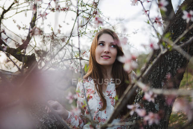 Гілки квітучого фруктового дерева і чуттєва молода жінка, дивлячись в природу — стокове фото