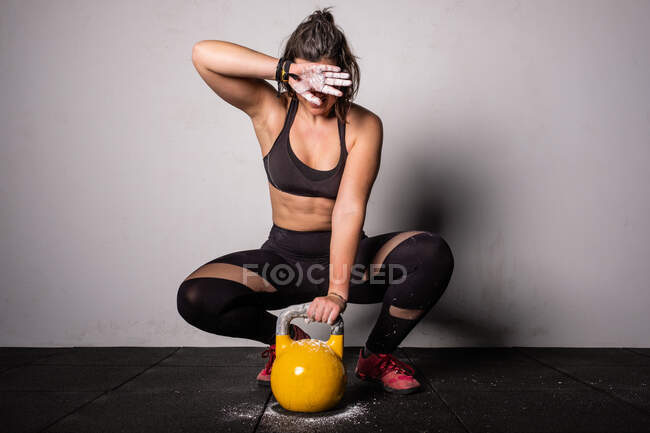 Atlética joven mujer concentrada en ropa deportiva subiendo kettlebell en el gimnasio - foto de stock