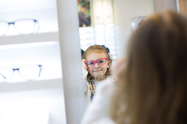 Carino ragazza cercando su occhiali in un negozio di occhiali — Foto stock