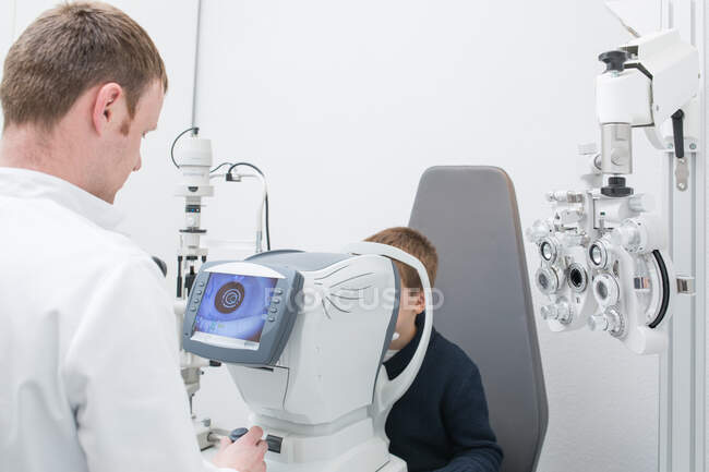 Ottico testare gli occhi di un ragazzo con dispositivi di optometria — Foto stock