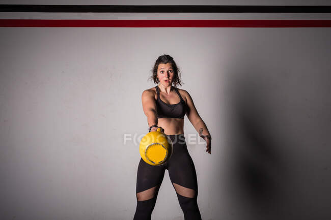 Спортивна молода концентрована жінка в спортивному одязі підвищує чайник у спортзалі — стокове фото