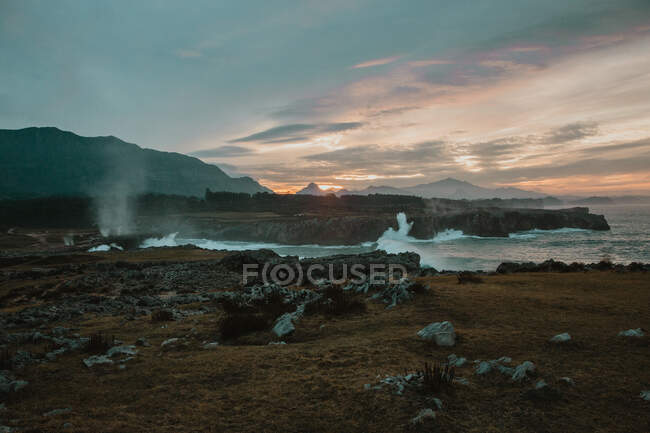 Picturesque view of high shore near stormy sea and beautiful cloudy sky at sunset in Bufones de Pria, Asturias, Spain — Stock Photo