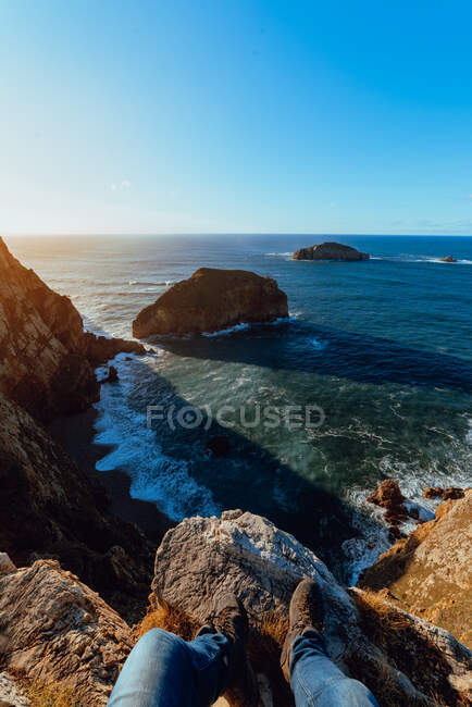 Menschenbeine auf einem Steinhügel in der Nähe des malerischen Meeres an sonnigen Tagen in Cabo de Penas, Asturien, Spanien — Stockfoto