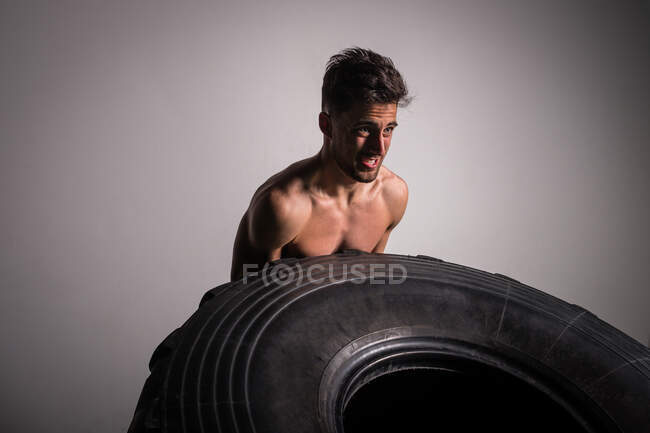 Athletic young shirtless guy having competition of flipping big tires in gym — Stock Photo