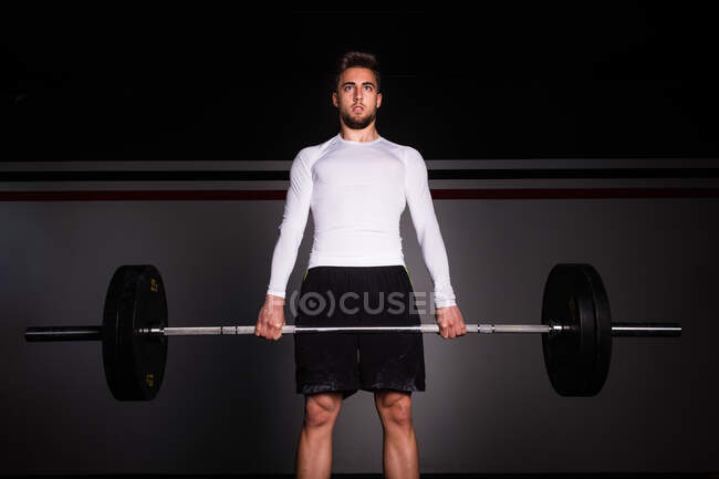 From below athletic young concentrated guy in sportswear upping barbell in gym — Stock Photo